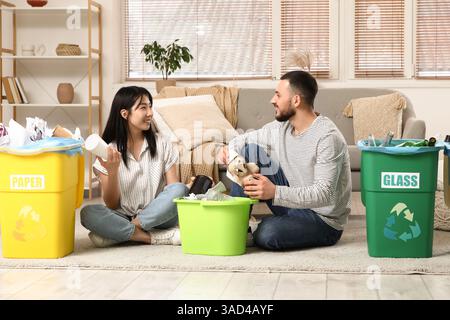 Young couple sorting rubbish in garbage bins at home. Global Recycling Day Stock Photo