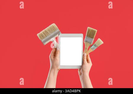 Female hands with paint brushes and blank tablet computer on red background Stock Photo