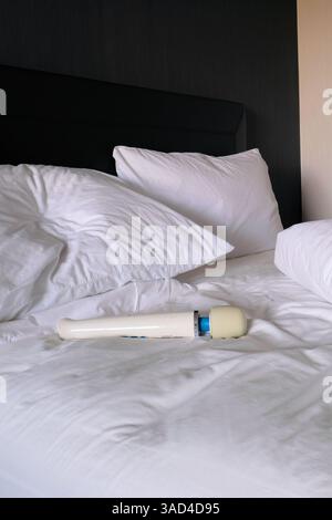 Cordless wand vibrator resting on an unmade hotel bed; travel companion for self-pleasure; masturbation. Stock Photo