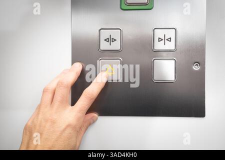 Elevator emergency call button used by passenger. Close up of woman pushing a button with a bell icon on stainless steel intercom. Call for help or st Stock Photo