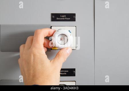 Old ceramic fuse inspected by technician or electrician. Hand on fuse in 4-story building. Depreciated electrical fuse cabinet to be replaced or updat Stock Photo