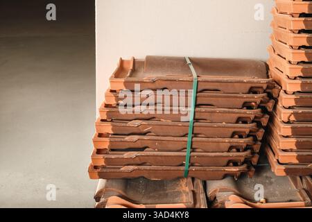 Spare roof tiles stored in attic or basement. Pile of orange and brown clay roof tiles kept for repair or replace broken roof parts. Clay roof shingle Stock Photo