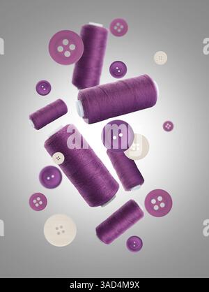 Many purple sewing threads and buttons falling on grey gradient background Stock Photo