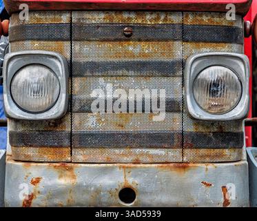 Detailed view of a weathered tractor front showing textured grill and aged headlights, reflecting years of outdoor use in a rural area. Stock Photo