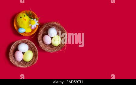 Lots of Easter eggs and a toy chicken in nests on a red background. Easter concept, close-up. Stock Photo