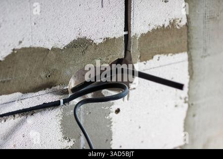 A collection of assorted wires is hanging down from a wall in a somewhat disorganized fashion, creating an intriguing visual effect Stock Photo