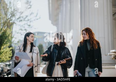 Three women walking and discussing project documents outdoors near a building Stock Photo