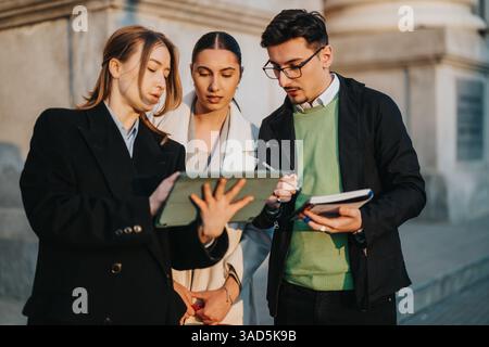 Three young professionals collaborating outdoors using a digital tablet for a project discussion. Stock Photo