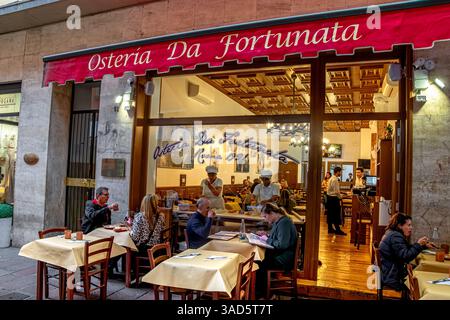 People making fresh pasta while people enjoy food sitting outside Osteria Da Fortunata an Italian restaurant on Via Altabella in Bologna,Italy Stock Photo
