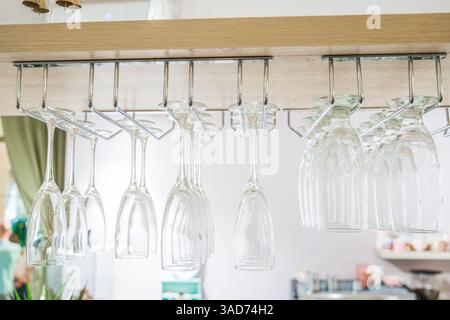 A row of wine glasses hanging from a rack. The glasses are all clear and are of various sizes Stock Photo