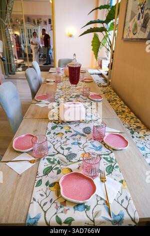 A table with a pink tablecloth and a floral pattern is set for a dinner party. There are several cups, forks, knives, and spoons on the table, as well Stock Photo