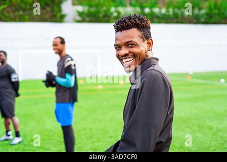 Portrait of young smiling black african man training in a football pitch, looking happy in camera. Young athlete practicing in a soccer field doing sp Stock Photo