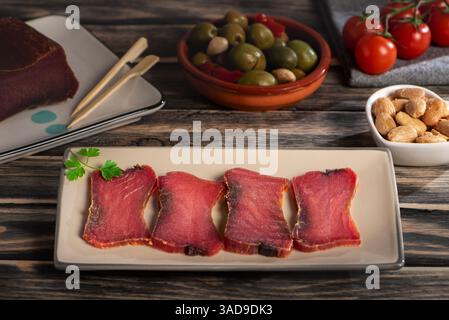 Slices of mojama, salt-cured tuna loin, accompanied by almonds, olives, and cherry tomatoes, a traditional dish from the coasts of Andalusia. Stock Photo