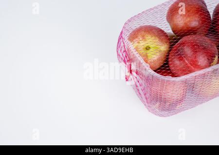 Plastic container of nectarines covered with red mesh in supermarket. Fresh juicy nectarines in plastic package to sell at farmer market isolated on w Stock Photo