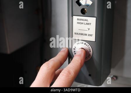 Person pushing reset button on hot water boiler. Natural gas boiler overheated or tripped. Female hand trying to restart the boiler. Hot water heating Stock Photo