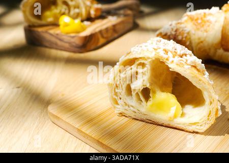 Close-up of sliced lemon croissant on a wooden cutting board. softly blurred croissant with lemon peel in the background Stock Photo