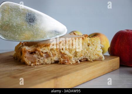 Piece of traditional thanksgiving apple cinnamon pie on the wooden cutting board with apples and walnuts on the white table. Homemade baked fruit tart Stock Photo