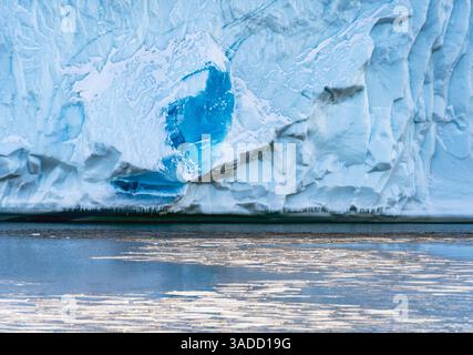 Close-up of a glacier with a striking blue ice formation, reflecting in calm water. The icy surface shows intricate textures and patterns, highlightin Stock Photo