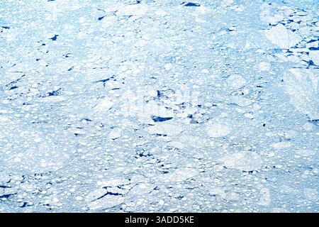 Aerial view of fragmented ice on a blue water surface, showcasing various shapes and sizes of ice pieces scattered across the water. Stock Photo