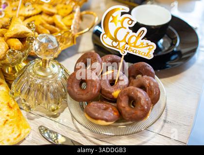 Plate of mini chocolate-glazed donuts with an Eid Mubarak sign on a beautifully set table. Festive sweets arranged for a joyful Eid celebration with Stock Photo