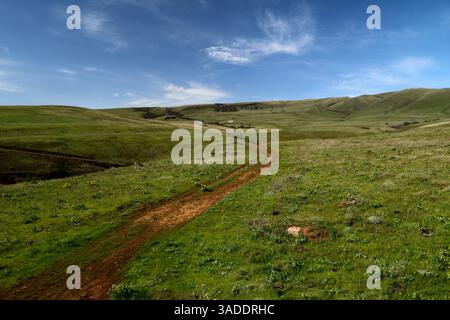 A path winding through green grassy hills with a blue sky above Stock Photo