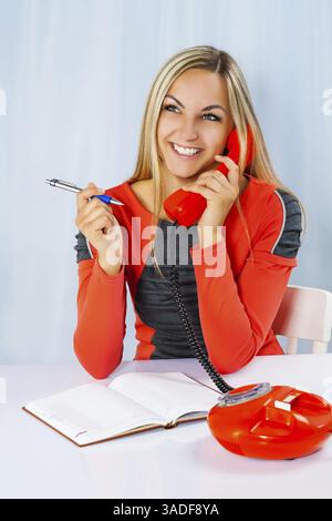 Beautiful smiling female holding phone and ballpoint pen Stock Photo