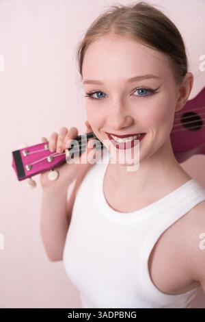 Young female musician holding ukulele by neck and slinging musical instrument over shoulder, she's feeling inspired. Beautiful woman looking camera wi Stock Photo