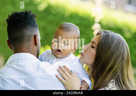 Multiethnic parents Biracial baby in park. Multiracial couple outdoor portrait. Biracial baby child with parents in backyard. Diverse family. African Stock Photo