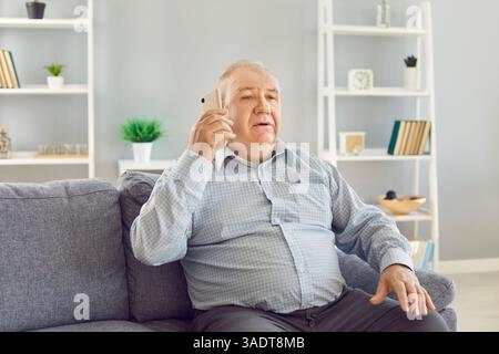 Portrait of senior confident man pensioner sitting on sofa at home and talking by smartphone Stock Photo
