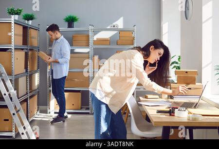 Man and a woman working in warehouse, inspecting cardboard boxes, preparing and packing orders. Stock Photo