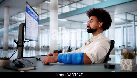 Recovering African Man Works On Computer After Arm Injury Stock Photo
