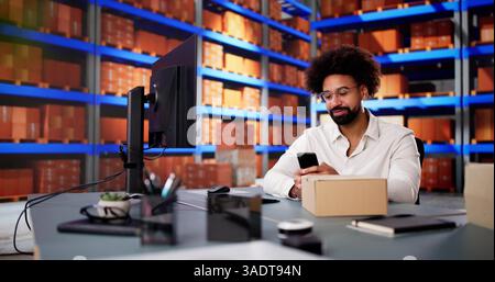 African American man scanning barcodes with smartphone in small office warehouse. Stock Photo