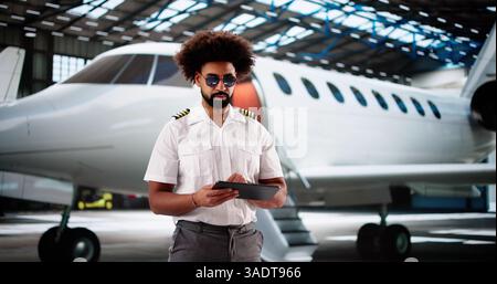 Professional African-American pilot smiling while using tablet for preflight maintenance. Stock Photo