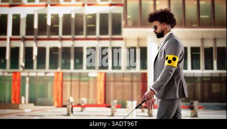 Young blind man wearing armband walks with white cane on sidewalk.   African American doctor chats with vision impaired businessman outside clinic Stock Photo