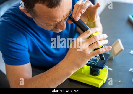 Man examining various samples under a microscope at home as a hobby. Concept of scientific curiosity and amateur microscopy Stock Photo
