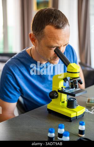 Man examining various samples under a microscope at home as a hobby. Concept of scientific curiosity and amateur microscopy Stock Photo