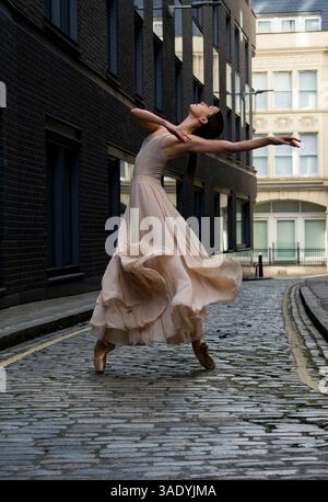 Ballerina dancing en pointe against an urban backdrop, elegant and graceful against the cobbled streets of London. Ballet dancer in pink skirts. London. Stock Photo