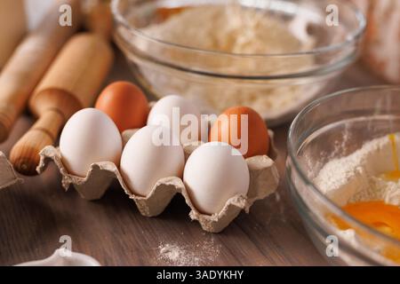 Fresh eggs in carton on rustic kitchen counter with flour and rolling pins, baking ingredients prepared. Stock Photo