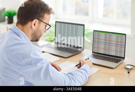 Busy focused analytics trader at desk looking laptop screen monitors for stock market data Stock Photo