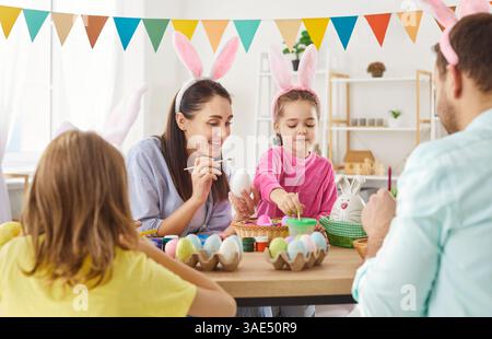 Happy friendly family gather together for decorating Easter eggs preparing at desk to celebrate Stock Photo