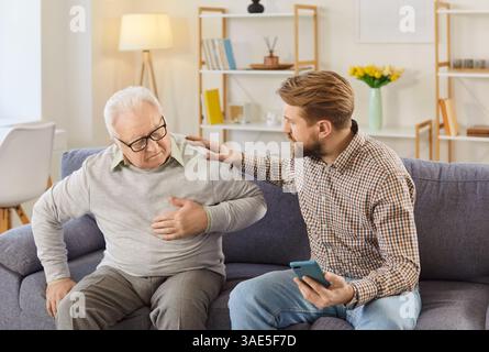 Worried man calling emergency ambulance to senior father suffering from heart attack at home. Stock Photo
