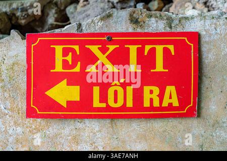 A close-up shows a red exit sign with Vietnamese translation, mounted on a weathered wall. It directs visitors to the exit. Stock Photo