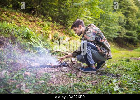 Young man lighting a fire in the forest during camping trip Stock Photo