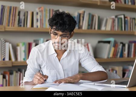 Young male student in glasses studying taking notes in library Stock Photo