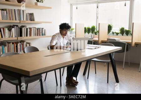 Busy male student engaged in learning at library using notebook Stock Photo