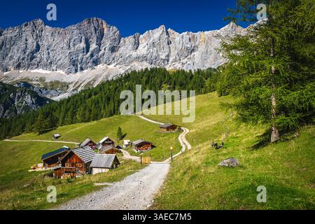 Beautiful hiking and travel place, cute alpine wooden houses on the green meadows. Southern walls of Dachstein mountains in background, Ramsau am Dach Stock Photo