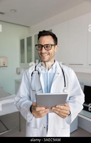 Smiling doctor dressed in white medical coat holding digital tablet Stock Photo