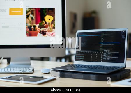 Laptop with codes on screen standing on workplace of programmer against computer with image generator in office Stock Photo