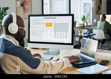 Young serious man in headphones pressing keys of laptop and desktop computer keypads while working over new software Stock Photo