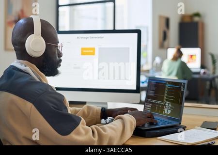 Young serious male office worker in headphones typing on laptop keypad while decoding data against screen with image generator Stock Photo